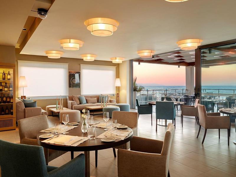 Elegantní restaurace s výhledem na západ slunce, moderním sezením a stoly s příbory a sklenicemi.