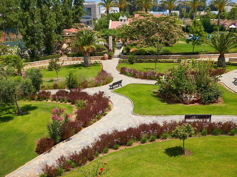 Zakrivené zahradní cesty s bujnými zelenými trávníky a různými keři za slunečného počasí.