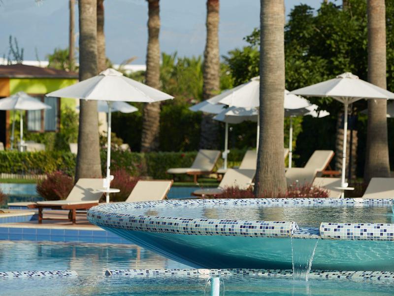 Okolí bazénu s lehátky, slunečníky a palmami v resortu.
