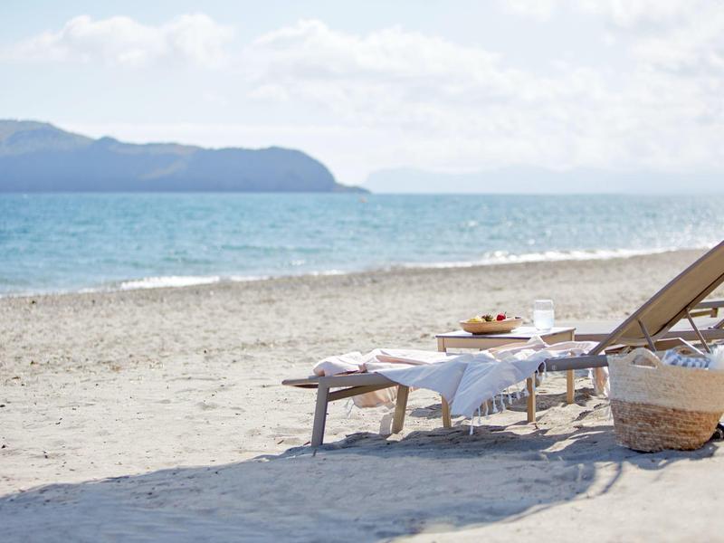 Plážová lehátka a stůl s věcmi připravenými k odpočinku u moře pod zataženou oblohou.
