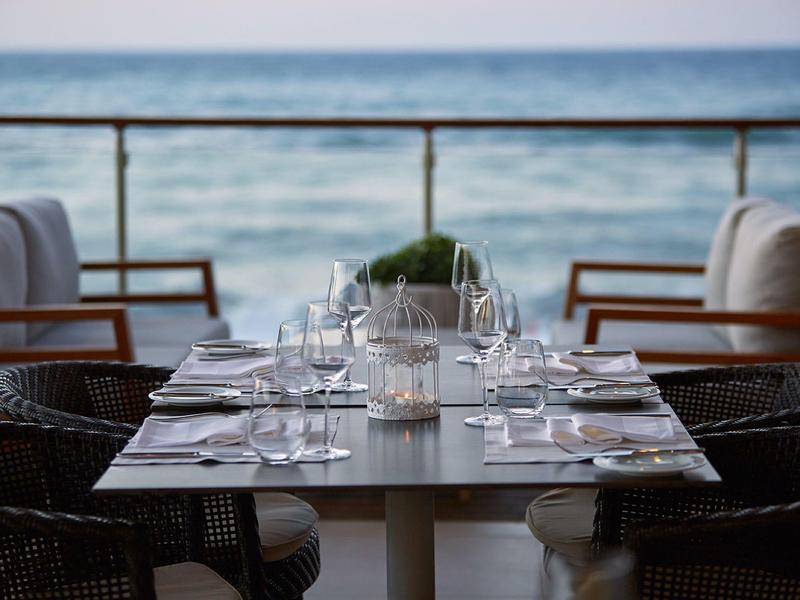 Venkovní jídelní stůl s židlemi s výhledem na oceán pod jasnou oblohou.