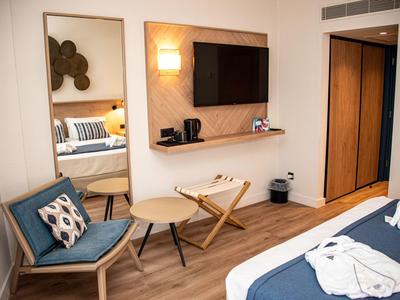 Camera d'hotel moderna con TV, zona salotto, grande specchio e pavimento in legno.