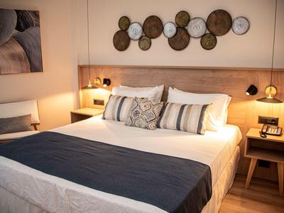 Camera d'hotel moderna con letto matrimoniale, cuscini decorativi e illuminazione calda sui comodini.