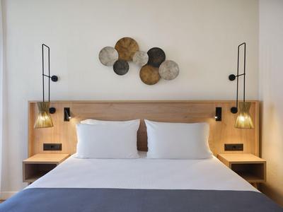 Camera d'hotel moderna con letto matrimoniale, testiera in legno, cuscini bianchi e decorazioni murali rotonde.