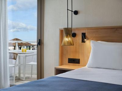 Camera d'hotel moderna con letto, pannello in legno e terrazza con vista mare