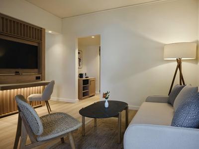 Area soggiorno moderna con divano, poltrone, tavolino e TV in ambiente illuminato caldamente.