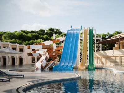 Diverse scivoli d'acqua accanto a una piscina con lettini e alberi sullo sfondo.