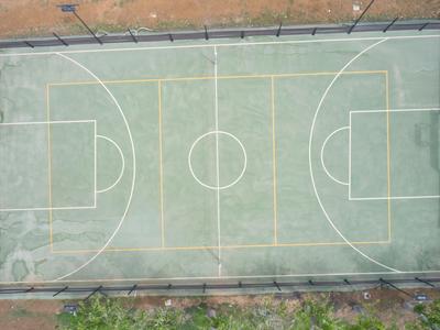 Campo da basket vuoto con linee bianche, circondato da recinzione e bordi verdi.