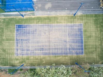 Vista aerea di un campo da tennis vecchio e consumato circondato da prato e marciapiede.