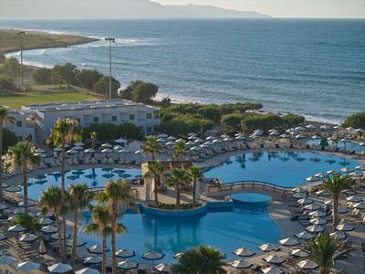 Grande piscina dell'hotel con palme accanto al mare sotto un cielo azzurro.
