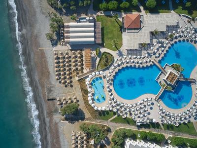 Vista aerea di un hotel sulla spiaggia con grande piscina, ombrelloni e lettini.