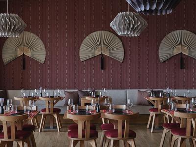 Sala da pranzo moderna con sedie in legno, cuscini rossi e ventagli decorativi di ispirazione asiatica sulla parete.