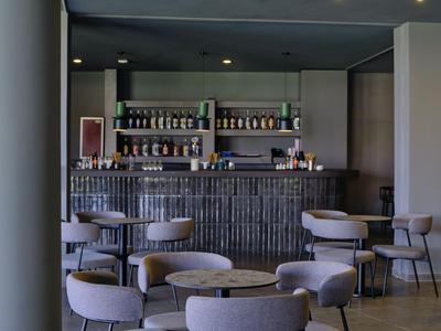 Area bar moderna con poltrone grigie e un bancone in legno in un hotel.