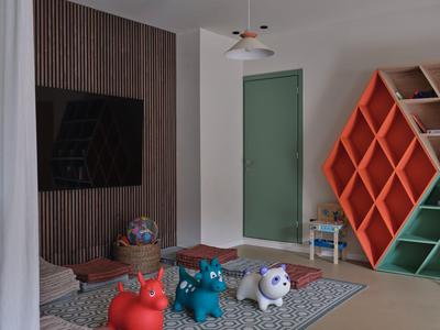 Una stanza moderna con parete in legno, cuscini a forma di animale e scaffali colorati accanto a una porta verde.