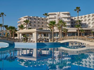 Hotelanlage mit großem Pool und mehreren Palm Bäumen unter klarem blauem Himmel.