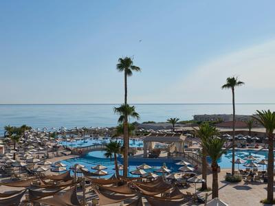 Blick auf einen Hotelpool mit Sonnenschirmen und Palmen am Meer bei klarem Himmel.
