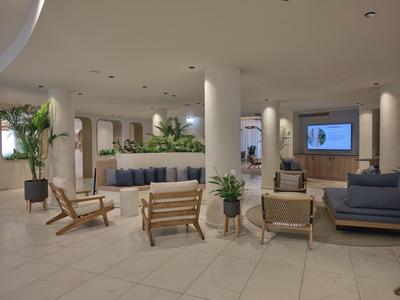 Moderner Hotel-Loungebereich mit Sesseln, Sofas und grünen Pflanzen auf hell gefliestem Boden.