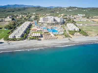 Hotelanlage mit Poolbereich und direktem Zugang zum Strand, umgeben von grünem Land und Bergen im Hintergrund.