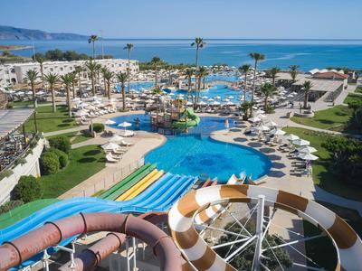 Blick auf einen Wasserpark mit Rutschen, Pools und Liegestühlen am Meer.