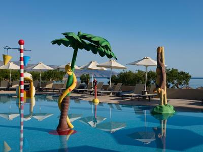 Bunter Pool mit künstlerischen Skulpturen und Sonnenschirmen vor klarem Himmel am Hotel