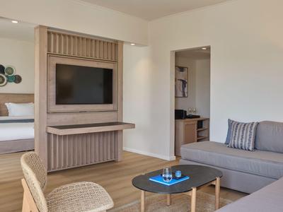 Modernes Hotelzimmer mit Sofa, Fernseher und Blick ins angrenzende Schlafzimmer.