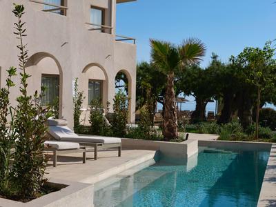 Moderner Poolbereich mit Liegestühlen vor einem hellen Gebäude und Palmen im Hintergrund.