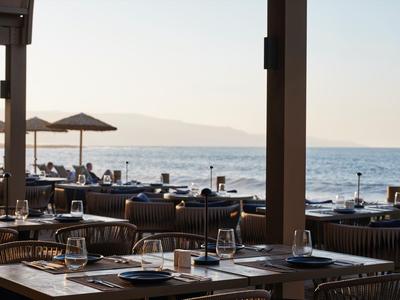 Blick auf gedeckte Tische und Stühle mit Meerblick und Sonnenschirmen bei Sonnenuntergang.