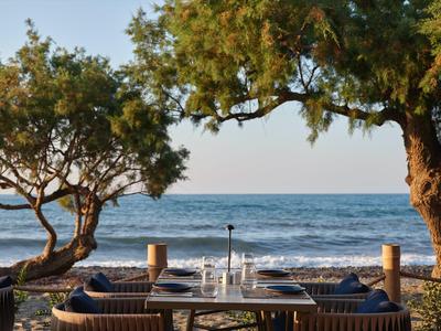 Table de plage dressée avec des couverts et des arbres avec vue sur la mer au coucher du soleil.