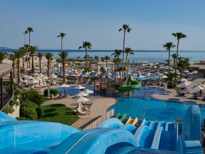 Parc aquatique avec toboggans, piscines, palmiers et vue sur la mer par jour ensoleillé.