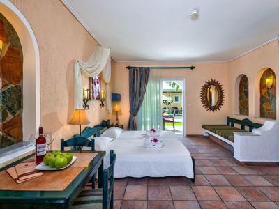 Lichte hotelkamer met tweepersoonsbed, balkon, terracotta vloer, decoratieve spiegel en tv.