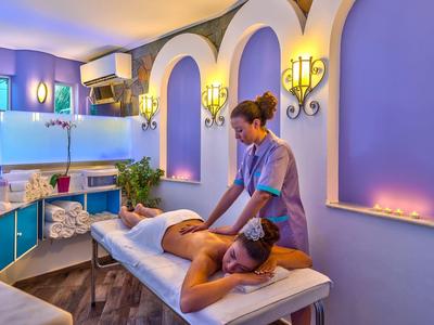 Vrouw krijgt massage in een rustige wellnessruimte met paarse verlichting en boogdecoratie.