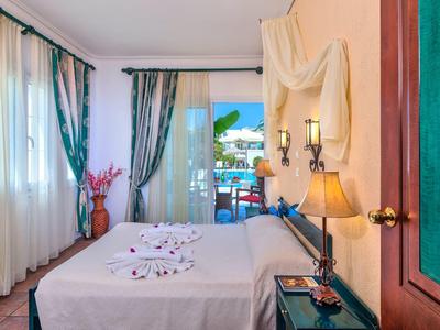 Lichte hotelkamer met tweepersoonsbed, decoratieve stof aan de muur en balkon met zeezicht.