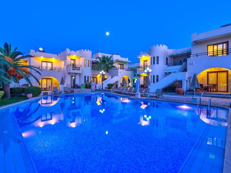 Verlicht hotel met groot zwembad en palmbomen 's nachts.