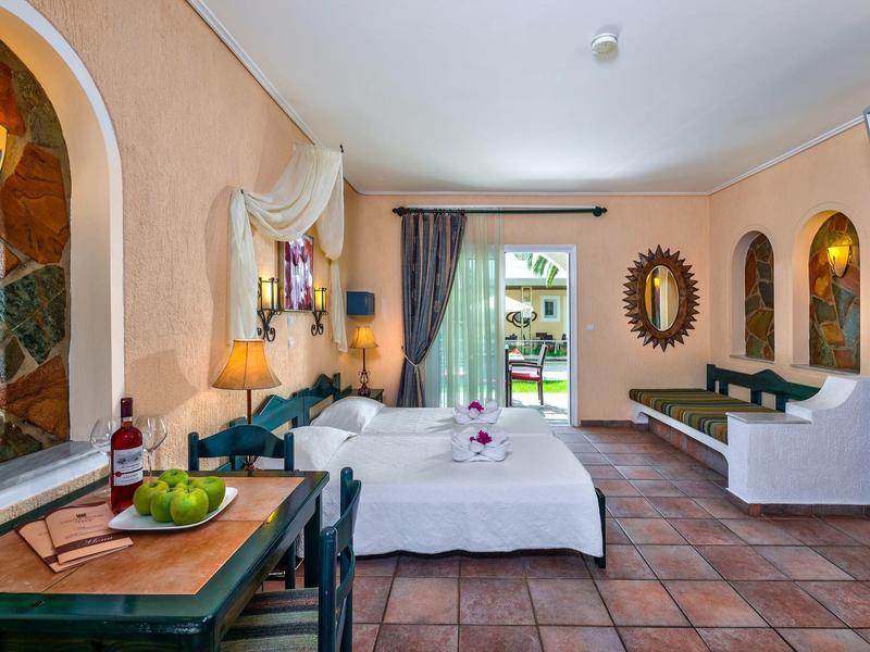 Lichte hotelkamer met tweepersoonsbed, balkon, terracotta vloer, decoratieve spiegel en tv.