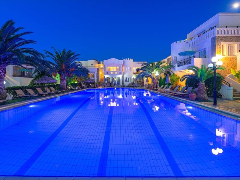 Verlicht hotelzwembad met ligstoelen en palmbomen 's nachts onder een heldere lucht.