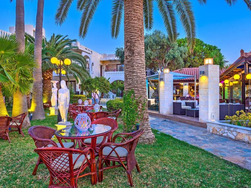 Tuin met rode stoelen en tafels onder palmbomen in een rustige avondsetting.