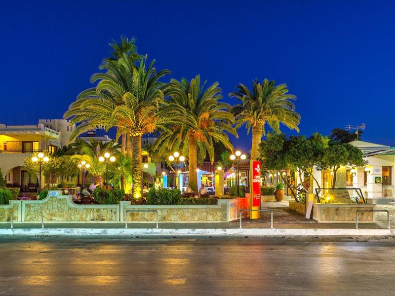 Verlichte hotelomgeving met palmbomen en zitgedeeltes 's nachts.