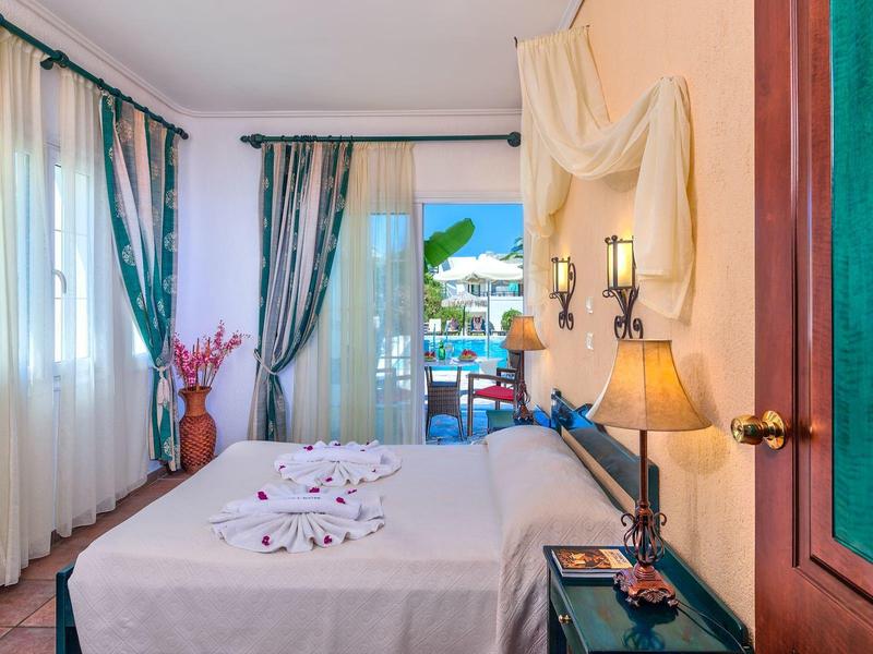 Lichte hotelkamer met tweepersoonsbed, decoratieve stof aan de muur en balkon met zeezicht.