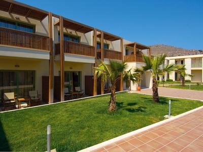 Hotel con camere su due piani, prato e palme sotto un cielo azzurro.