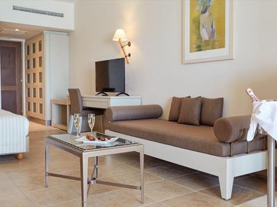 Area della camera d'hotel moderna con divano, TV, letto e piccolo tavolo con vino e snack.