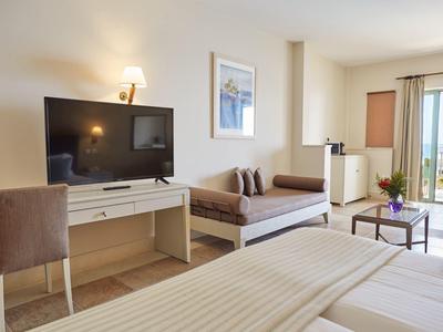 Camera d'hotel luminosa con letto matrimoniale, scrivania, divano e balcone con vista sul mare.