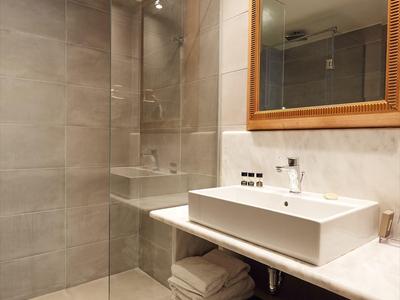 Bagno moderno con doccia a filo, lavabo bianco e grandi piastrelle grigie.