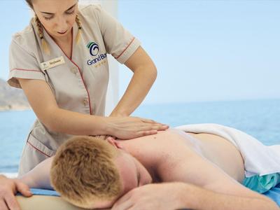 Massaggiatore che fa un massaggio alla schiena a una persona sulla spiaggia con cielo sereno e mare.