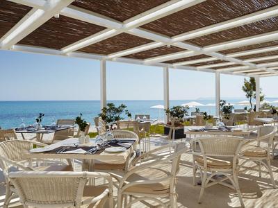 Offenes Restaurant mit Blick auf das Meer, hell und luftig mit Rattanstühlen und gedeckten Tischen.