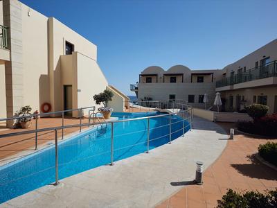 Moderner Hotelpoolbereich mit klar blauem Wasser und umliegenden Gebäuden unter blauem Himmel.