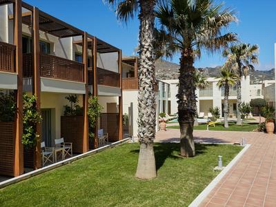 Moderner Hotelkomplex mit Zimmern, Palmen und gepflegtem Rasen unter klarem blauem Himmel.