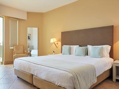 Camera d'hotel luminosa con letto grande, comodini e sedia vicino alla finestra