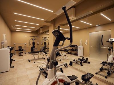 Heller Fitnessraum mit verschiedenen Trainingsgeräten und neutraler Einrichtung.