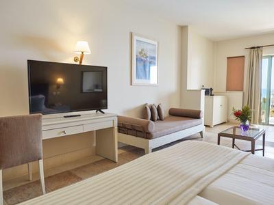 Camera d'albergo luminosa con letto matrimoniale, divano, scrivania, TV e balcone con vista.