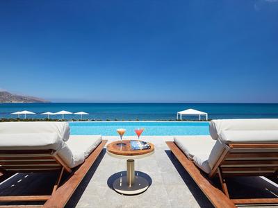 Zwei Liegestühle mit Getränken am Meer unter blauem Himmel und weißen Sonnenschirmen.